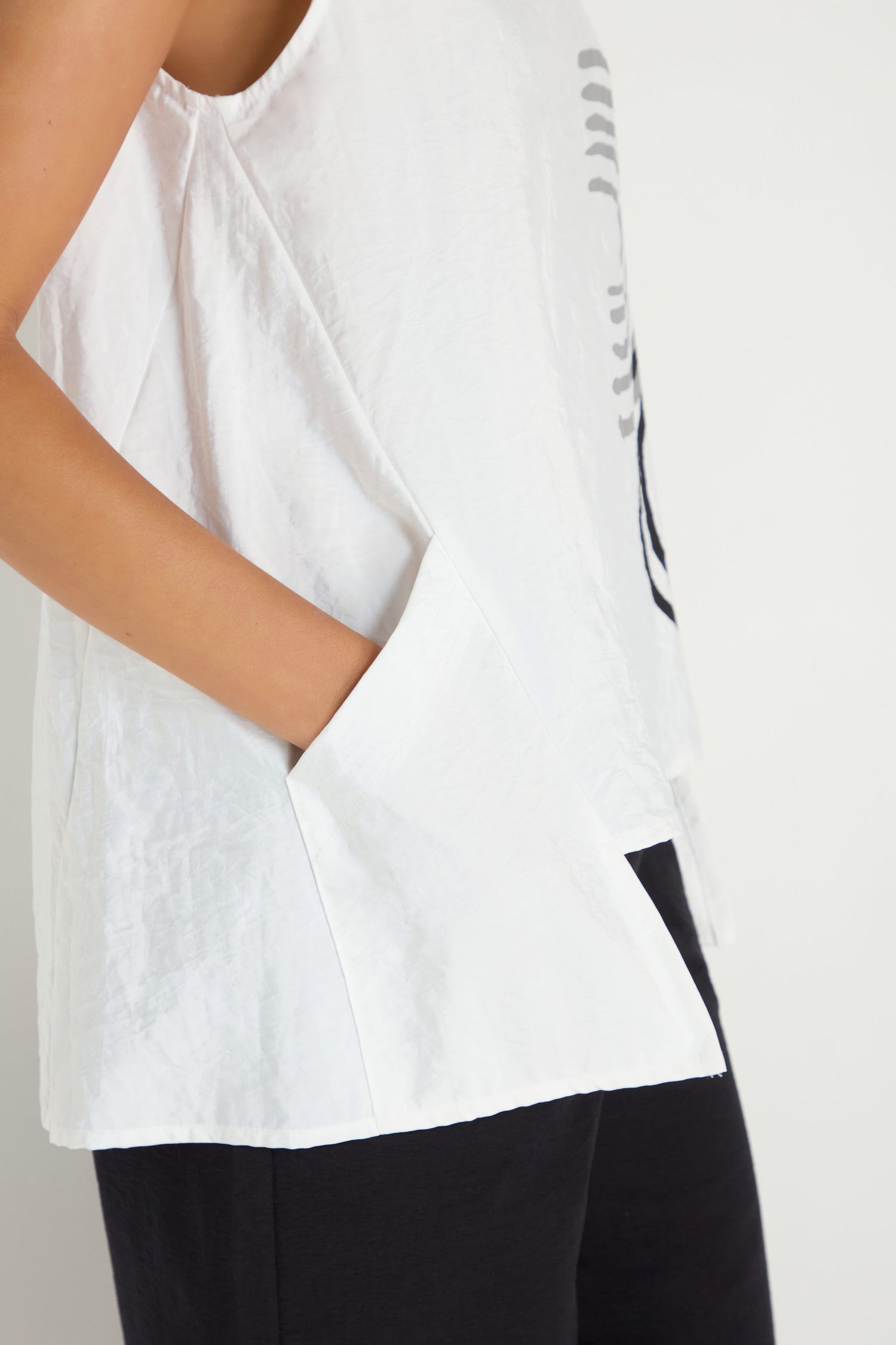 A person wears the Roll Collar Step Hem Top, a sleeveless white piece with large pockets, paired with black pants, standing against a plain background.