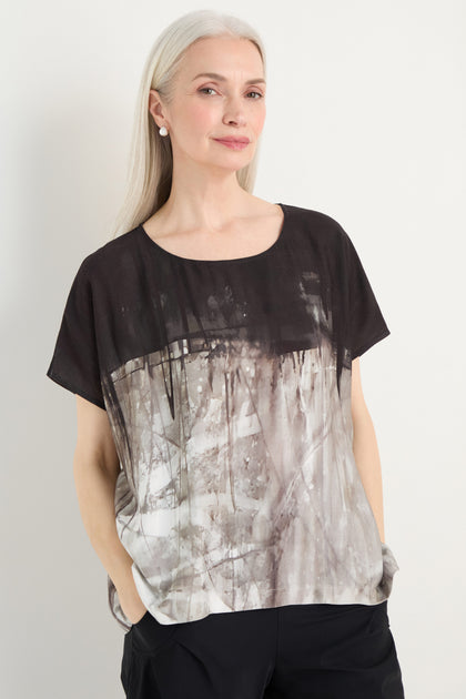 A woman with long gray hair wears the Abstract Print Easy Top in black and gray, paired with black pants, standing with her hands in her pockets against a plain background.
