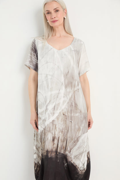 Woman with long gray hair wears the Abstract Print Bubble Dress, featuring a relaxed fit and a white, gray, and black abstract pattern, standing against a plain white background.