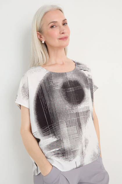 A woman with long gray hair stands against a white background, wearing the Shaded Print Top and light gray pants.