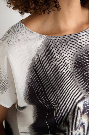 A woman with long, straight gray hair models the Shaded Print Top—a relaxed-fit piece with abstract black and white monochrome designs—standing before a plain light background.