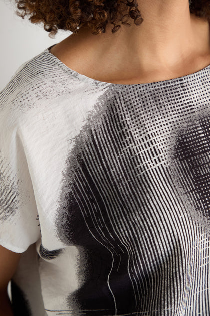 A woman with long, straight gray hair models the Shaded Print Top—a relaxed-fit piece with abstract black and white monochrome designs—standing before a plain light background.