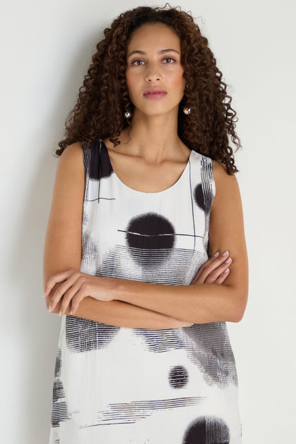 Woman with curly hair stands with arms crossed in a Shaded Print Flared Dress—a monochrome, midi-length dress featuring black abstract patterns—against a light background.