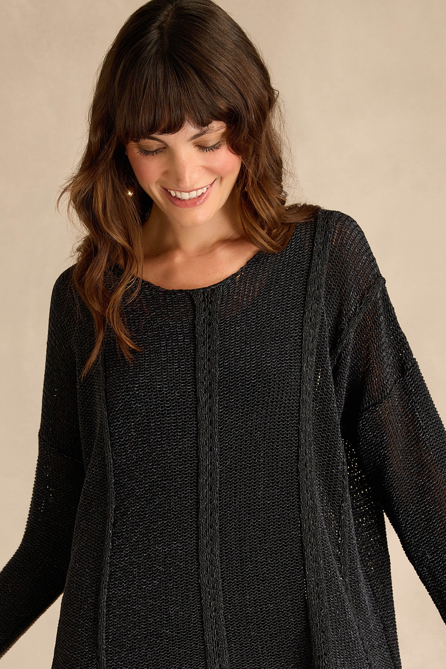 A woman with wavy brown hair smiles as she looks down, wearing the Black Seam Detail Scoop Neck Knit against a neutral background.
