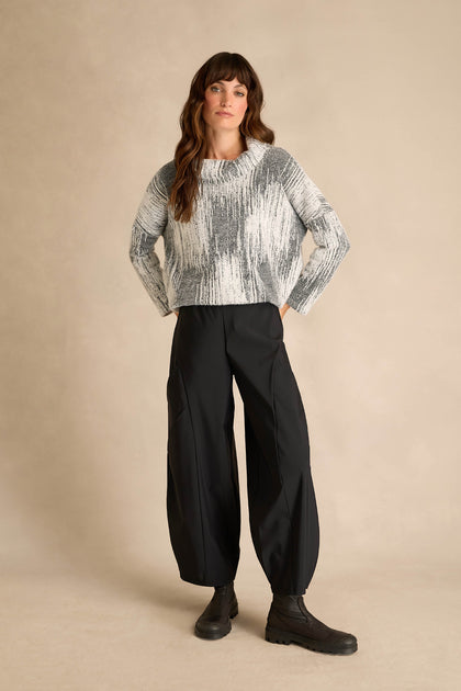 Person standing against a beige background, wearing a gray and white knit sweater, Seamed Bubble Trousers in black, and black boots.