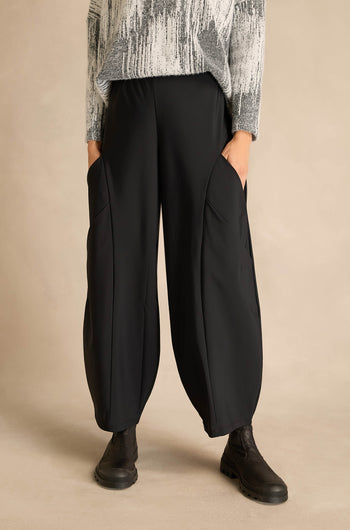 A person wearing Seamed Bubble Trousers with large pockets, a black and white textured sweater, and black boots stands against a plain beige background.