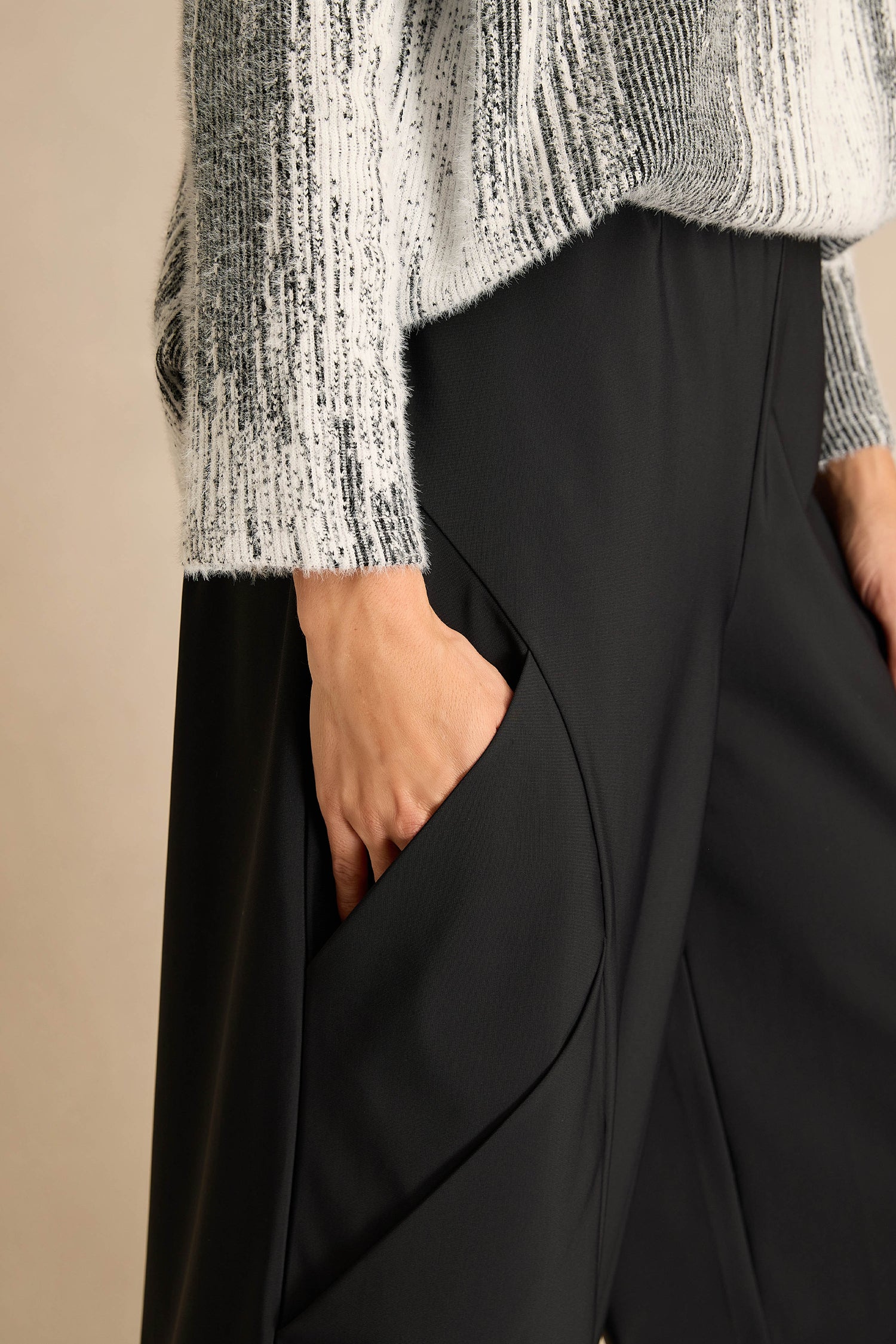 A person wearing a textured gray and white sweater and black Seamed Bubble Trousers has their right hand in their pocket.