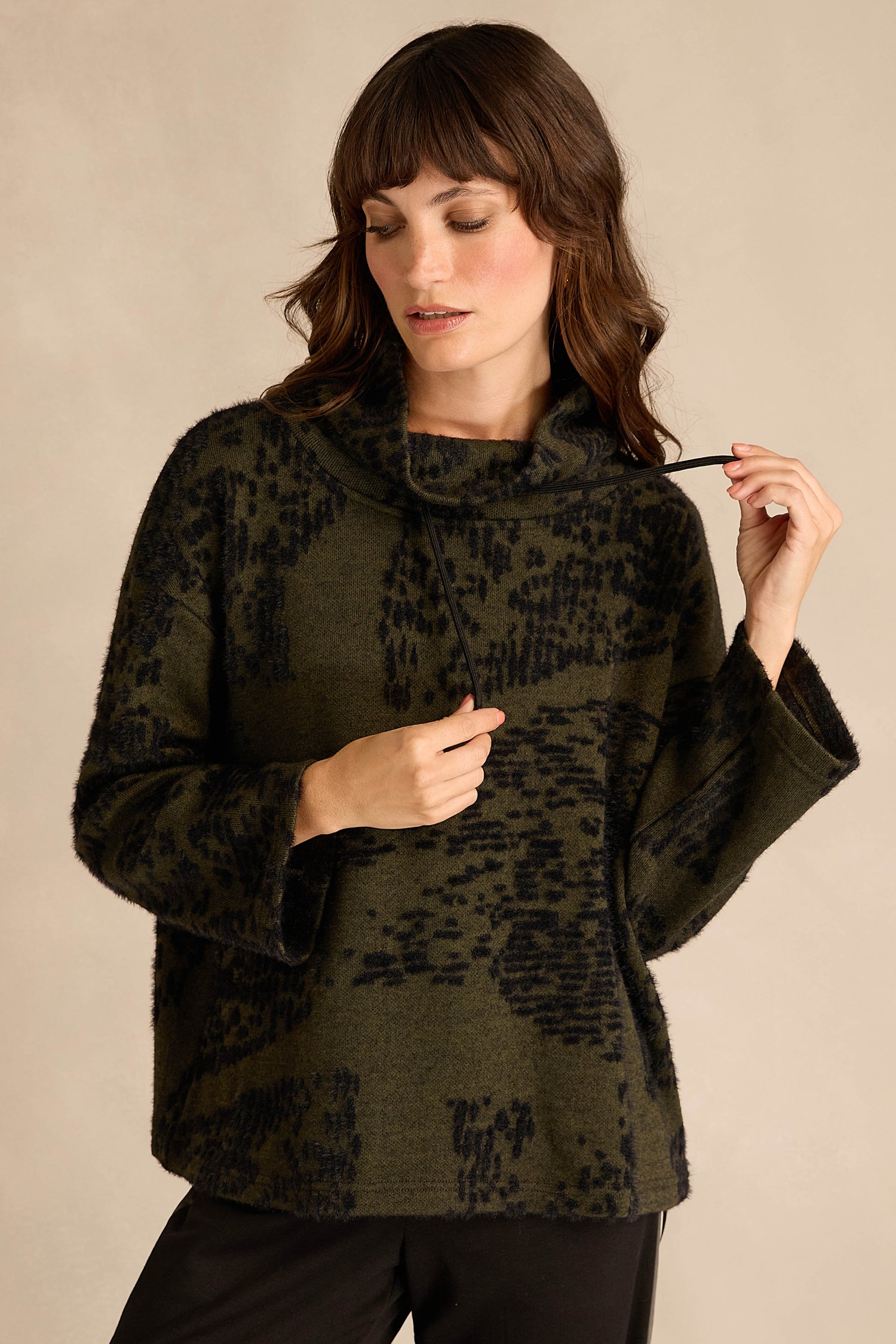 Woman wearing the Thyme Speckled Jersey Boxy Top, featuring a textured dark green and black pattern, boxy fit, and wide sleeves, looking down while holding one side of the collar.