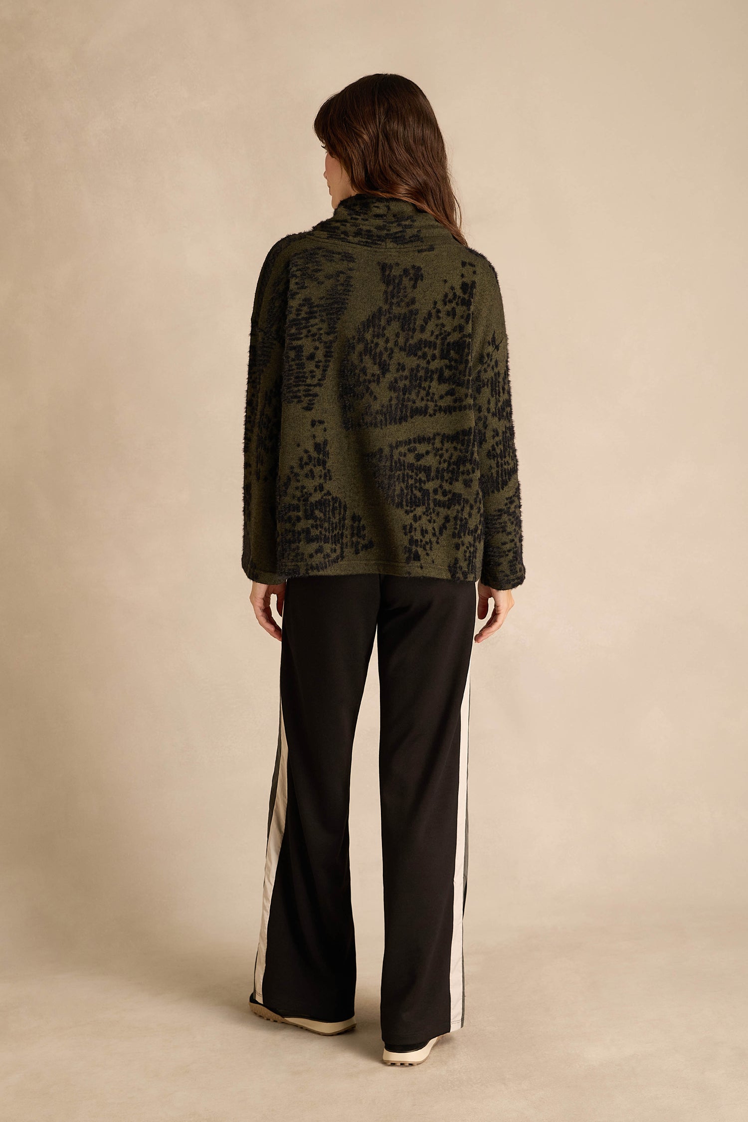 A person stands with their back to the camera, wearing the Thyme Speckled Jersey Boxy Top—a dark green, patterned jacket-style top—paired with black pants featuring white side stripes, set against a neutral background.