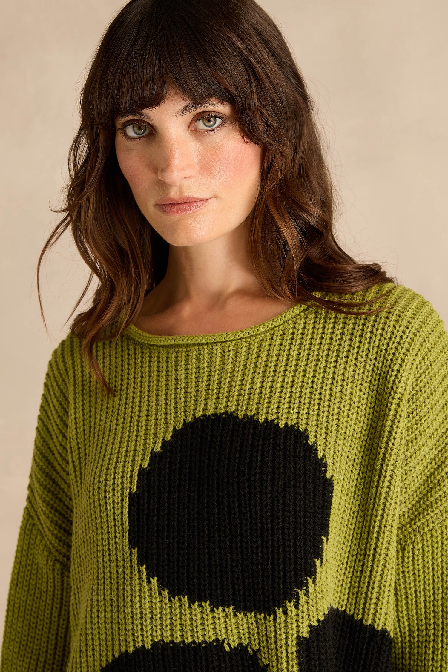 Woman with wavy brown hair wearing the Avocado Spot Scoop Neck Knit sweater, featuring large black dots, looking at the camera against a neutral background.