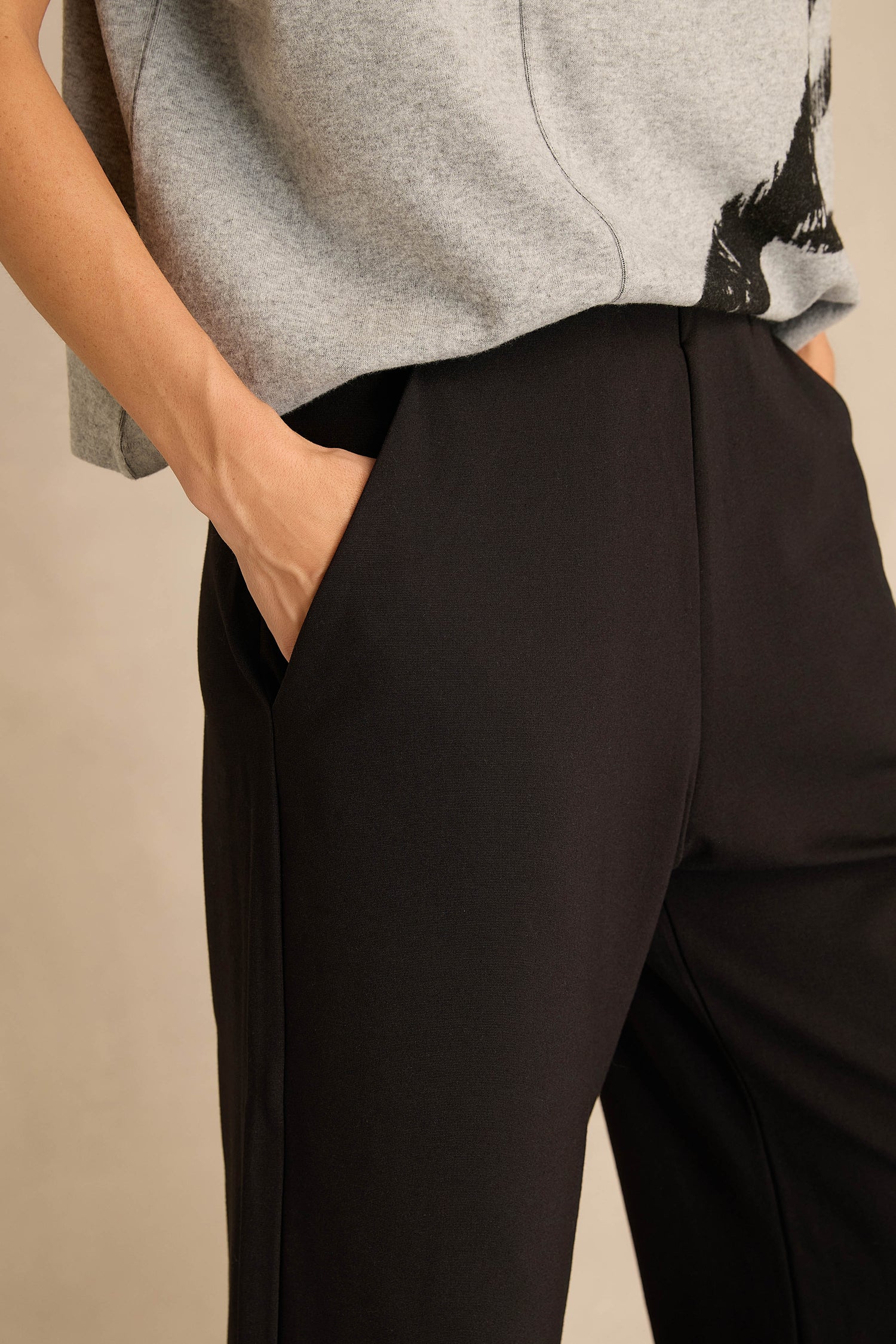 Person wearing a gray short-sleeve top and the Wide Leg Ponte Trousers in black stretch ponte jersey, with their right hand in the trouser pocket, shown from waist to mid-thigh.