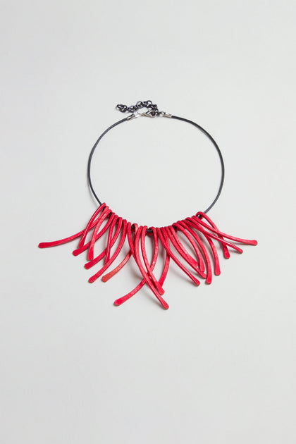 Introducing the Arc Necklace: a black choker featuring multiple curved red anodised aluminium elements fanned out at the front, secured with an adjustable metal clasp closure. This contemporary jewellery piece is crafted as wearable art, making a bold and striking statement.