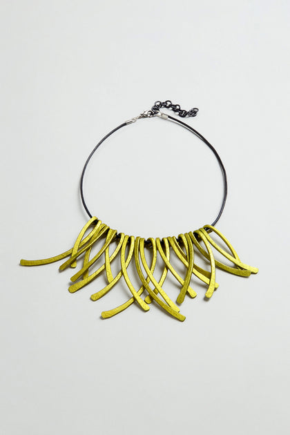 Discover the Arc Necklace: a striking piece of contemporary jewellery that serves as wearable art. Featuring a black chain and multiple curved, yellow-green pendants arranged in a dramatic fringe pattern, this necklace is expertly crafted from anodised aluminium to blend modern style with artistic flair.
