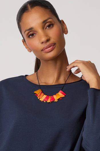 A person wearing a navy blue top and the Mini Segment Necklace poses for the camera, holding the contemporary piece in one hand.
