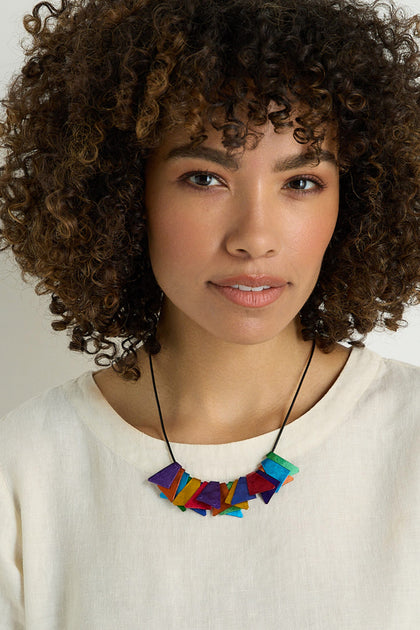 A woman with curly hair wears a cream-colored top and the Mini Segments Necklace, featuring colorful geometric shapes, as she looks directly at the camera with a neutral expression.