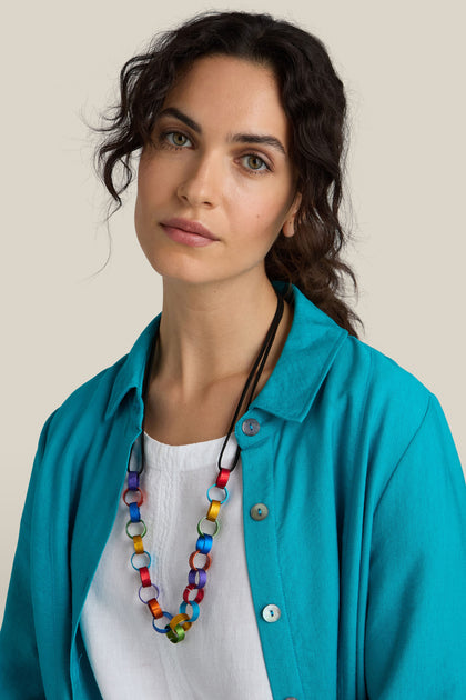 Person with curly hair wearing a teal shirt over a white top and the Rainbow Links Necklace, standing against a plain background.