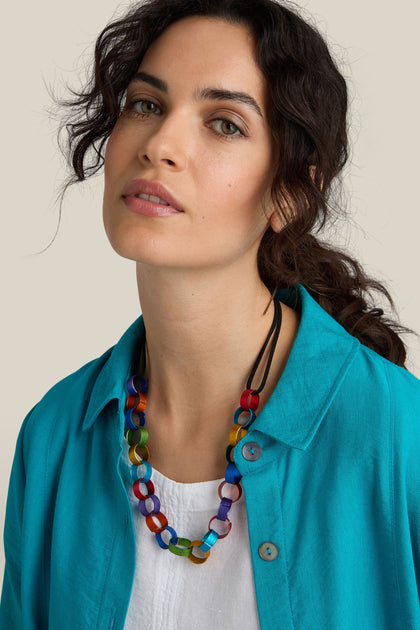 A person with wavy dark hair wearing a turquoise shirt and the Rainbow Links Necklace, featuring an adjustable cord, looks towards the camera with a neutral expression.