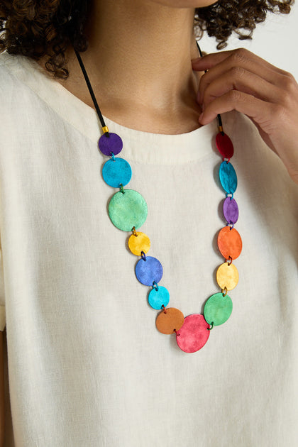A person wears a white top and the Colourful Aluminium Discs Necklace, which features large, vibrant, layered circular beads.
