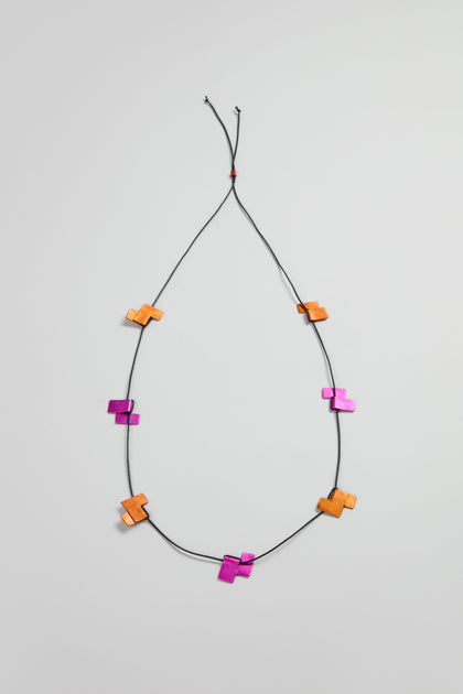 The Tetris Necklace is a black cord necklace with evenly spaced orange and magenta geometric wooden beads, showcasing a modern jewellery style against a simple light background.