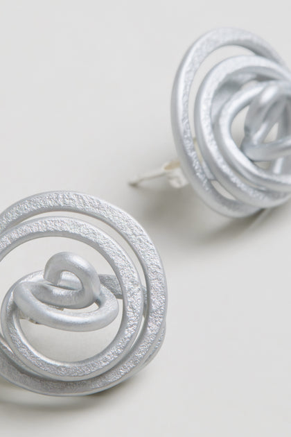 Close-up of the Mini Spiral Earrings, showcasing sculptural and abstract intertwined circular designs in anodised aluminium against a plain light background.