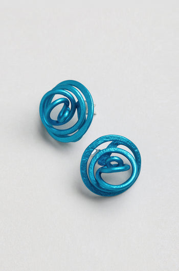 A pair of Mini Spiral Earrings in blue anodised aluminium, featuring circular shapes, abstract patterns, and a sculptural design, displayed on a plain light background.