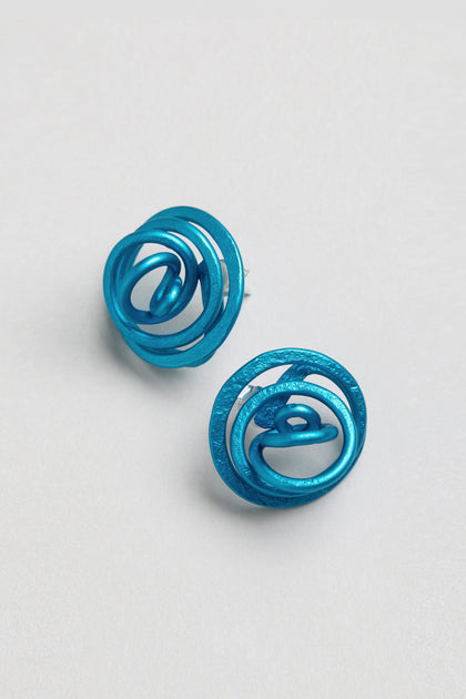 A pair of Mini Spiral Earrings in blue anodised aluminium, featuring circular shapes, abstract patterns, and a sculptural design, displayed on a plain light background.