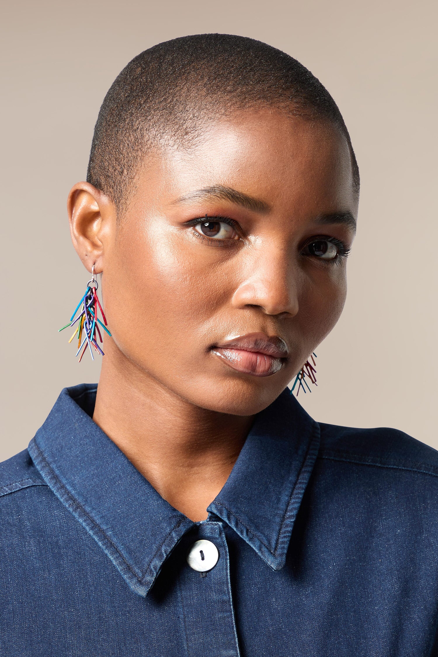 A black woman wearing a denim shirt and Fringe Earrings.