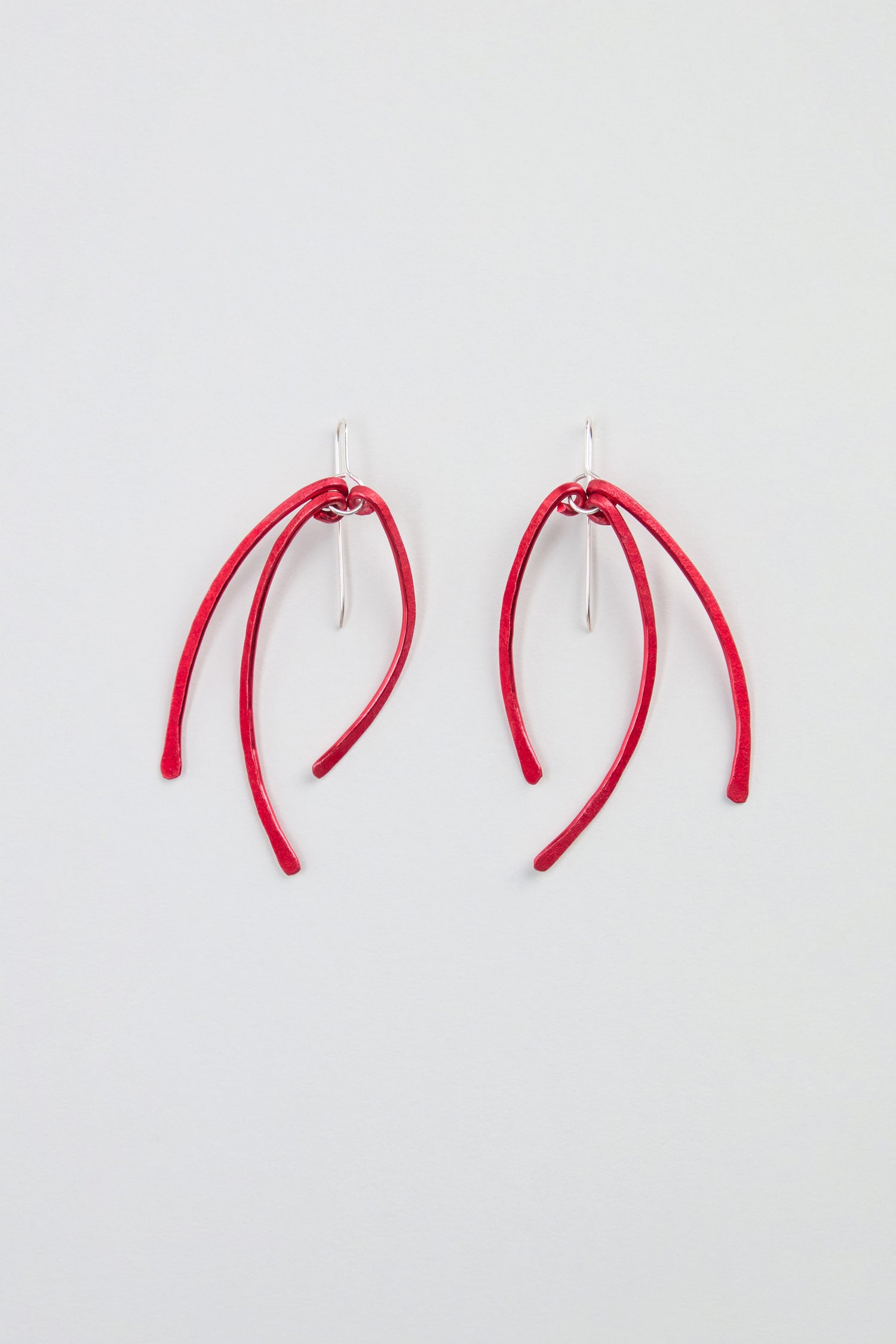 Arc Earrings – Crafted from anodised aluminium, these earrings feature three curved red stems suspended from sterling silver hooks, and are displayed on a plain white background.