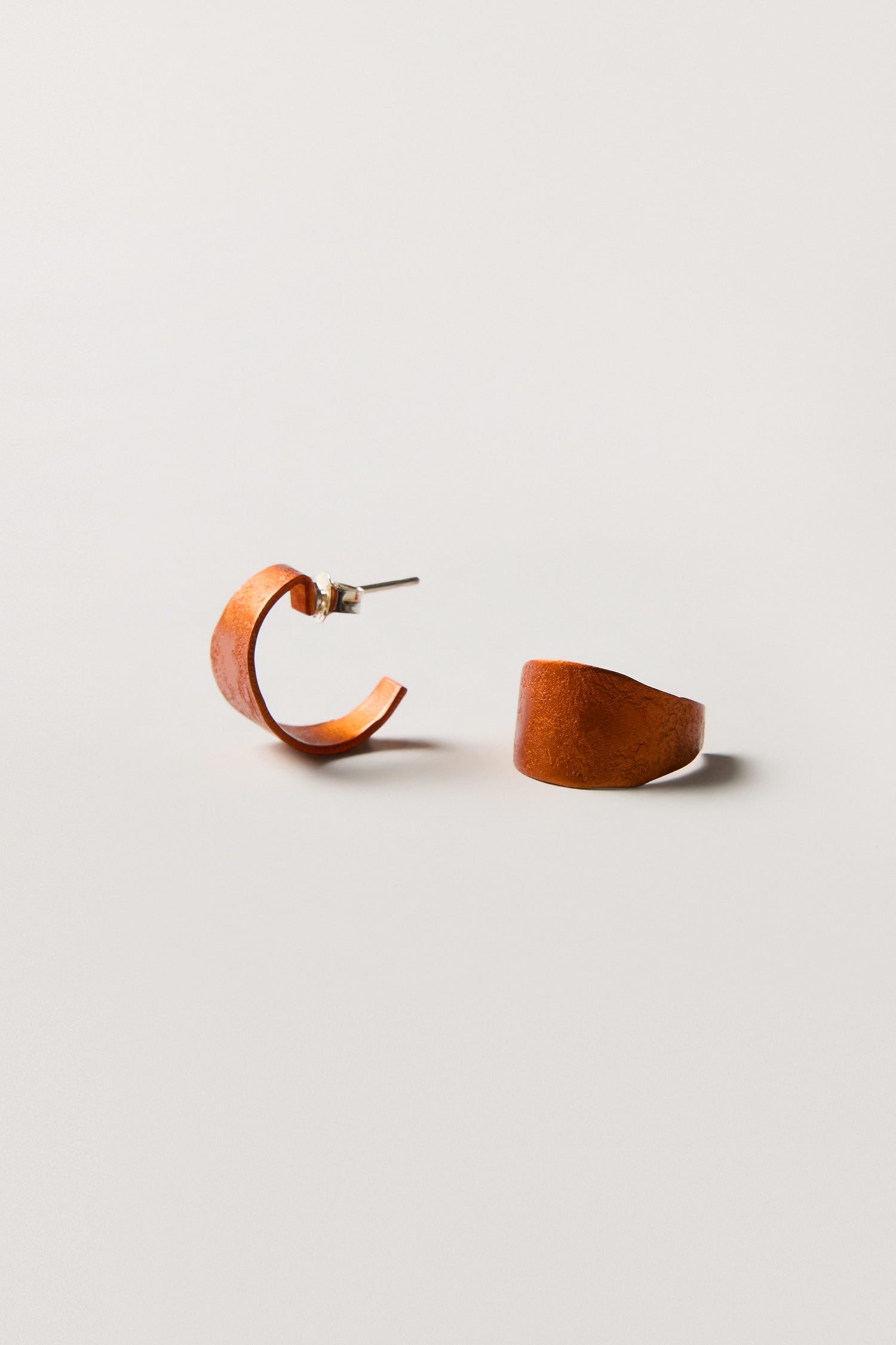 Two brown, semi-circular hoop earrings with a matte finish are displayed on a plain white background—an elegant pair of Curved Earrings perfect for those who love contemporary jewellery.