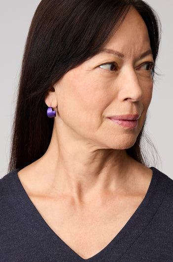 A woman with straight dark hair, wearing a navy V-neck top and Curved Earrings, looks to her right against a plain background—an elegant touch of contemporary jewellery.