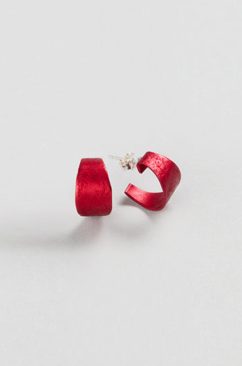 A pair of red Curved Earrings by Oana Millet with semi-circular design and silver posts, shown on a plain white background—ideal as contemporary jewellery and bold statement accessories.