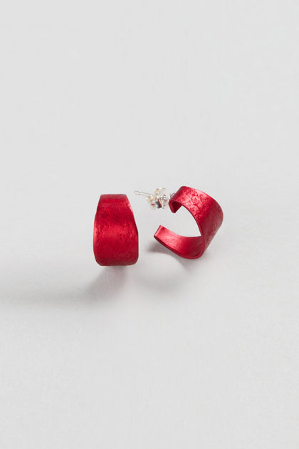 A pair of red Curved Earrings by Oana Millet with semi-circular design and silver posts, shown on a plain white background—ideal as contemporary jewellery and bold statement accessories.