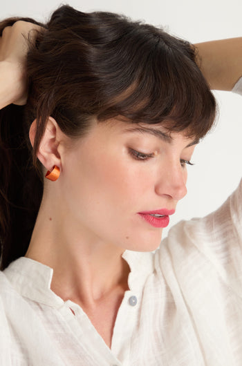 A woman with dark hair, in a white shirt, wears Curve Earrings in anodised aluminium as she looks down and holds up her hair against a plain background.