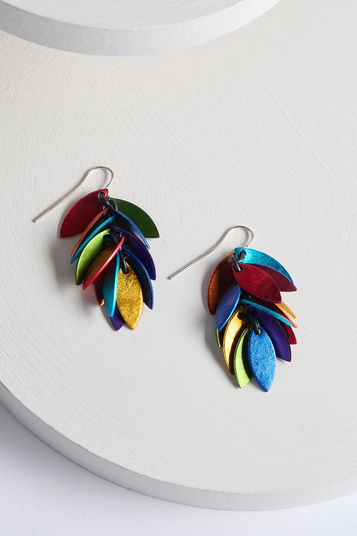 The Scattered Leaves Earrings from a Spanish design studio feature colorful, dangling pieces crafted from layered aluminium in vibrant red, green, blue, yellow, and orange leaf shapes.