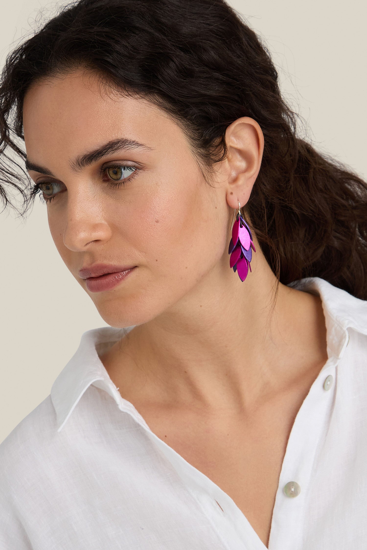 Woman with dark hair wearing a white shirt and the distinctive Scattered Leaves Earrings, designed by a Spanish design studio. She is looking slightly to her left against a plain, light background.