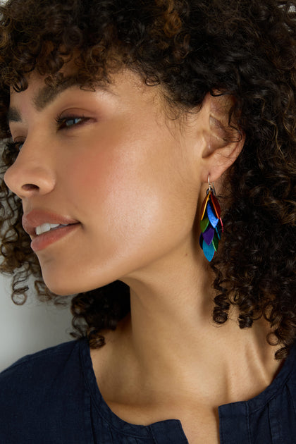 Woman with curly hair wearing a dark blue top and Scattered Leaves Earrings—lightweight, colorful drop earrings featuring layered leaf shapes in anodised aluminium.