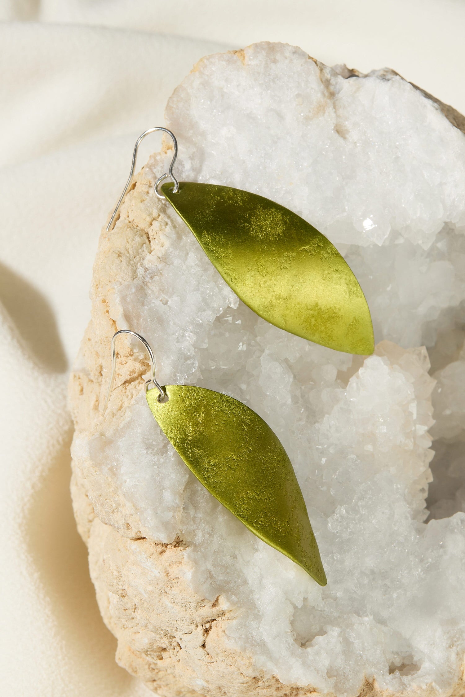 A pair of Leaves Earrings on a rock, featuring silver hooks.
