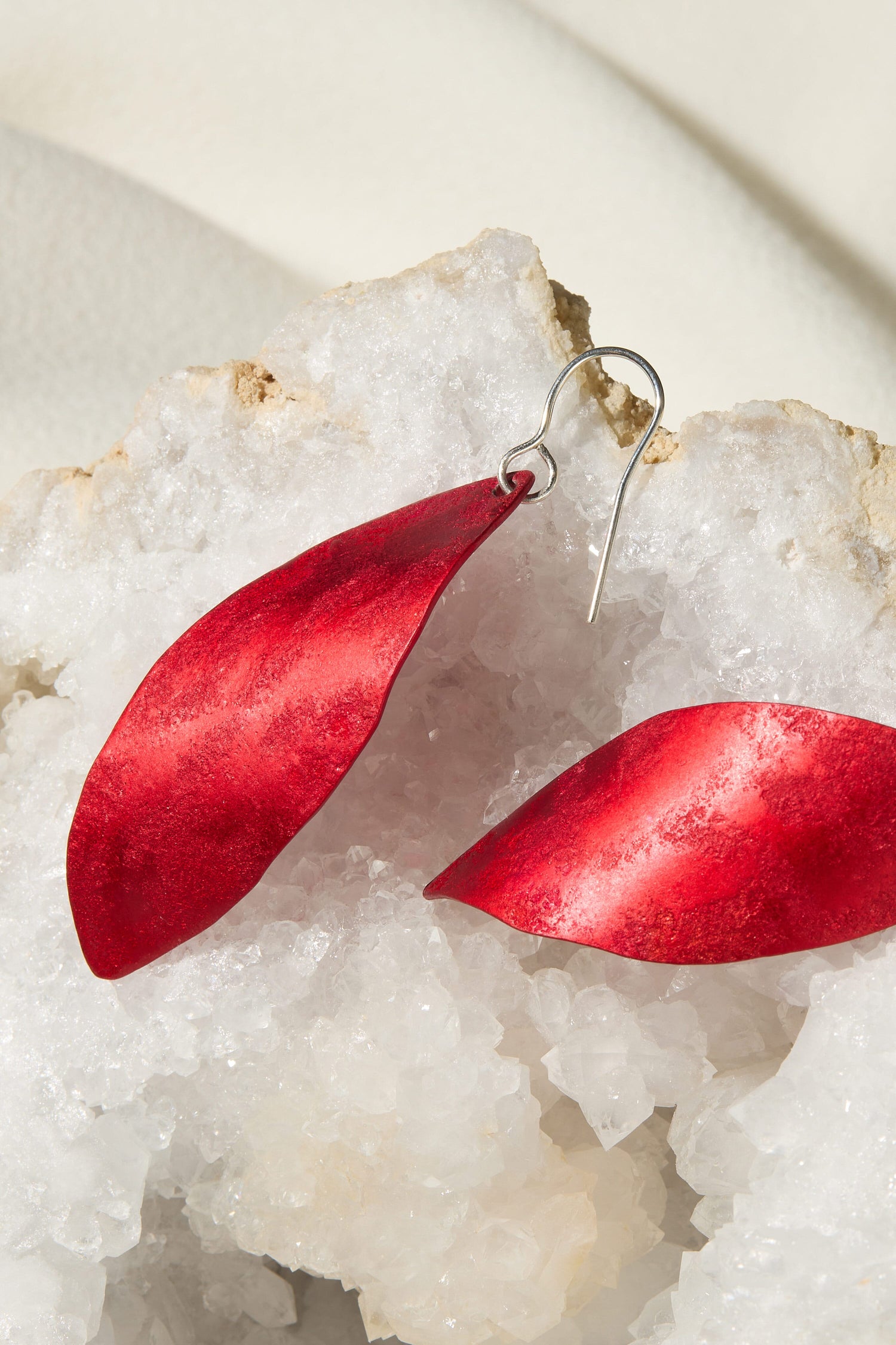 A pair of red Leaves Earrings, featuring silver hooks, sitting on top of a rock.