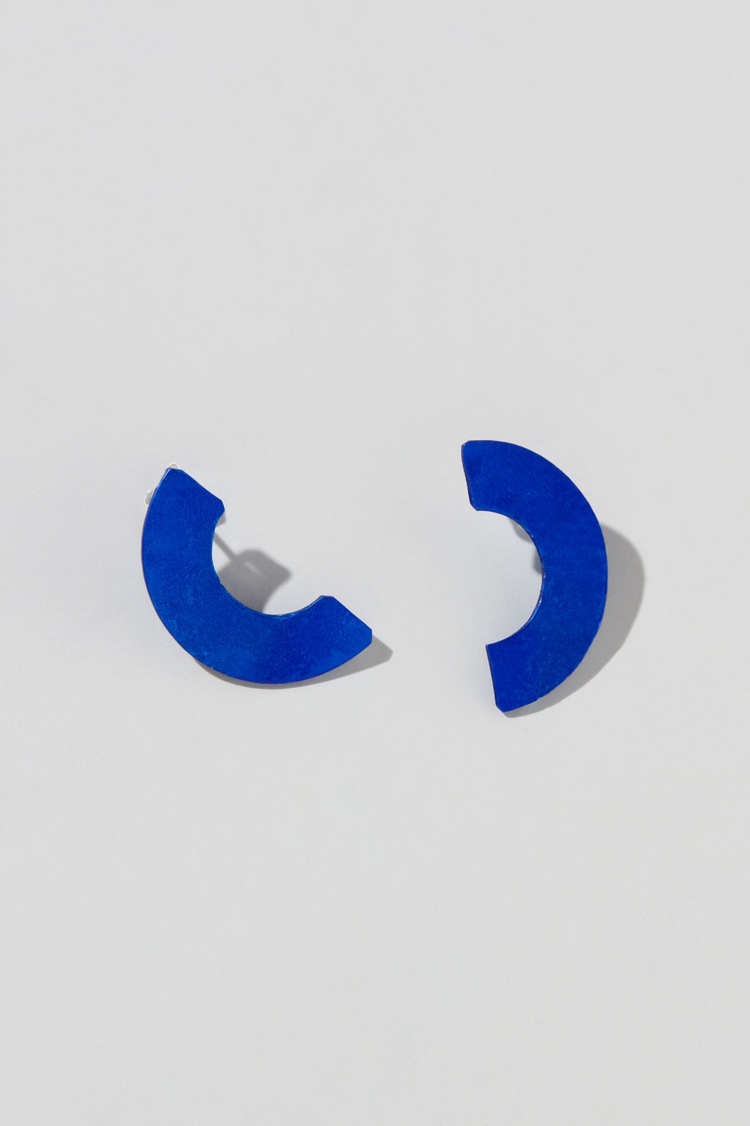 Two Aluminium Crescent Earrings face each other on a light gray background, capturing the sleek design of the OAE399.