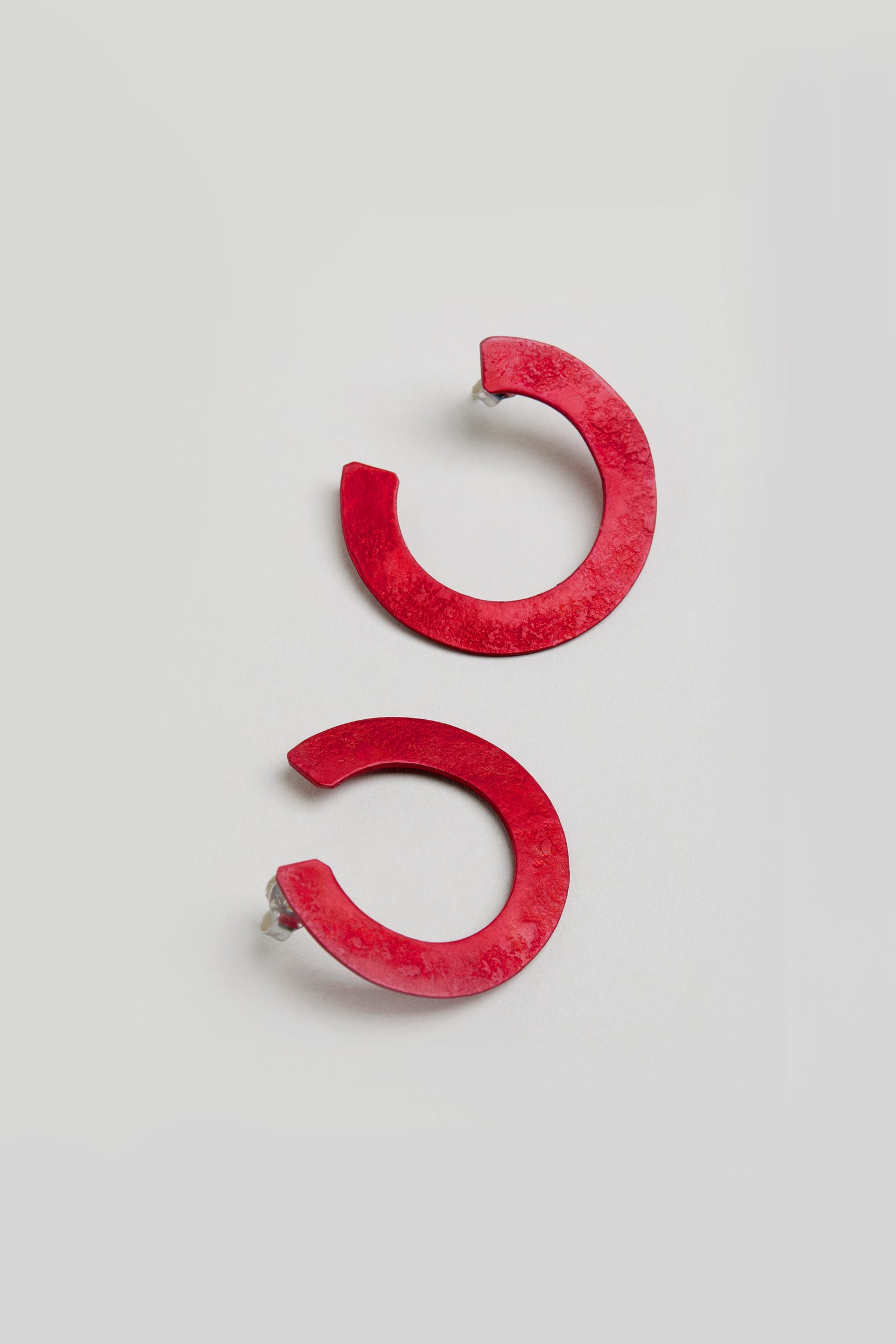 The C Curve Earrings are bold, red, semi-circular hoops with post backs, shown on a light background—modern accessories designed for a standout look.