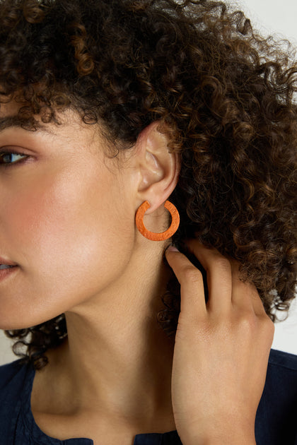 A person with curly hair touches a C Curve Earring on their left ear, with part of their face and hand visible against a neutral background.