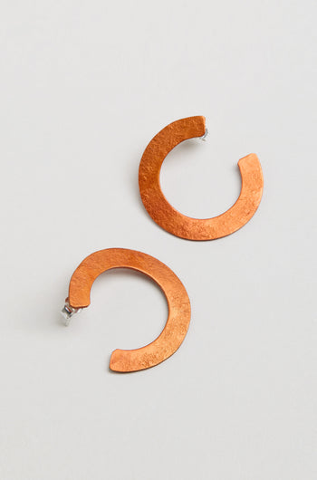 The C Curve Earrings feature a modern hoop shape in a distinctive C design, crafted from textured copper-colored metal and shown against a plain light background.