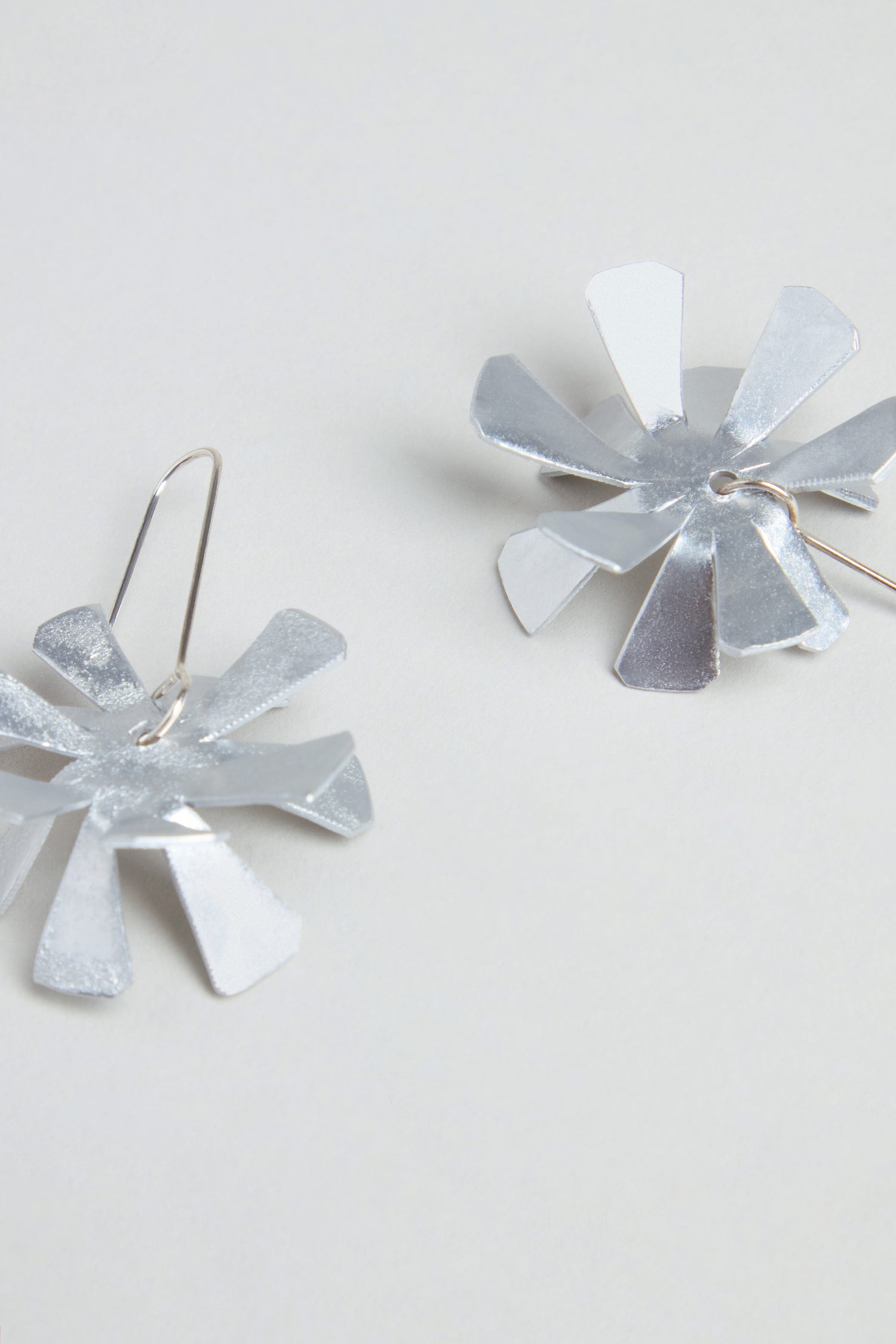The Flower Earrings feature silver metallic, petal-like segments and sterling silver hooks, displayed on a light background.