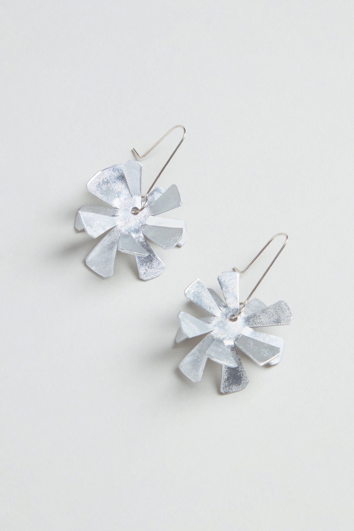 Flower Earrings: Silver metallic floral design crafted from anodised aluminium with sterling silver hooks, shown on a light grey background.