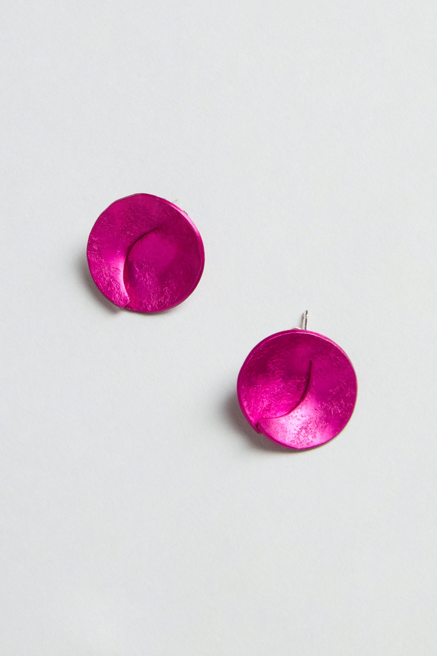 Curved Disc Earrings: round, textured metallic pink anodised aluminium with sterling silver posts, shown on a plain light background.