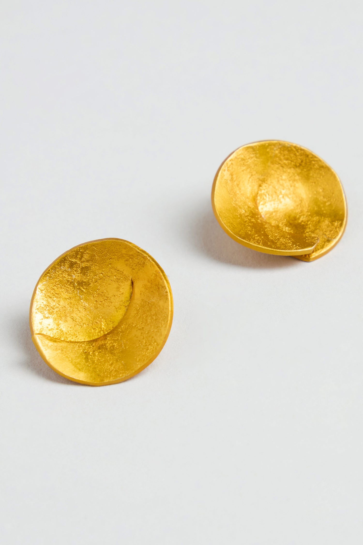 A pair of Curved Disc Earrings featuring round, textured gold discs and sterling silver posts, shown on a plain white background.