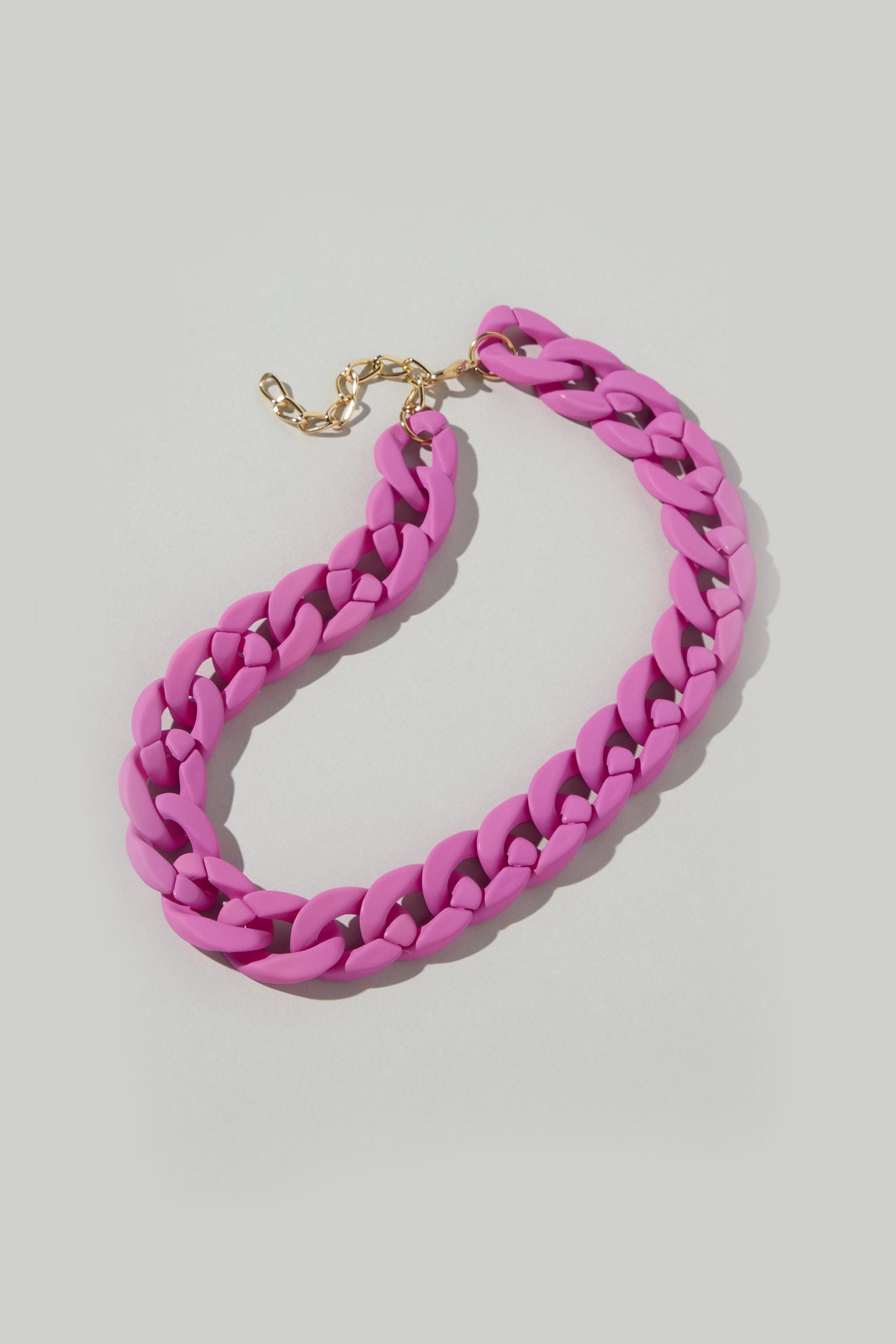 A chunky pink chain necklace with a gold clasp rests on a light gray background, making it the ideal Colour Pop Link Necklace to enhance any outfit.