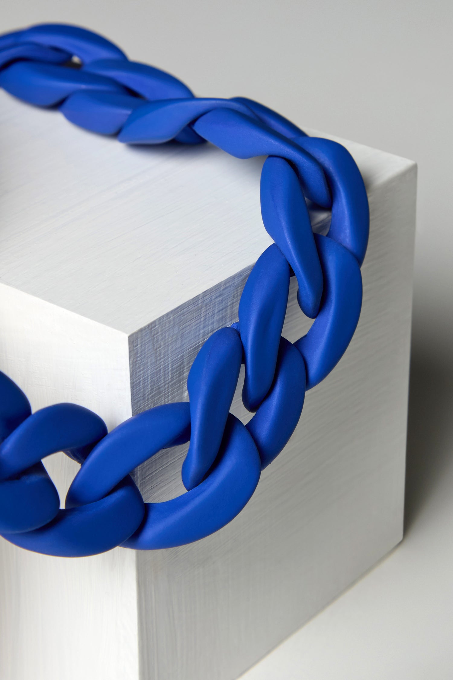 The Colour Pop Link Necklace, with a chunky blue chain and adjustable gold clasp, is showcased draped over a white rectangular block on a neutral background.