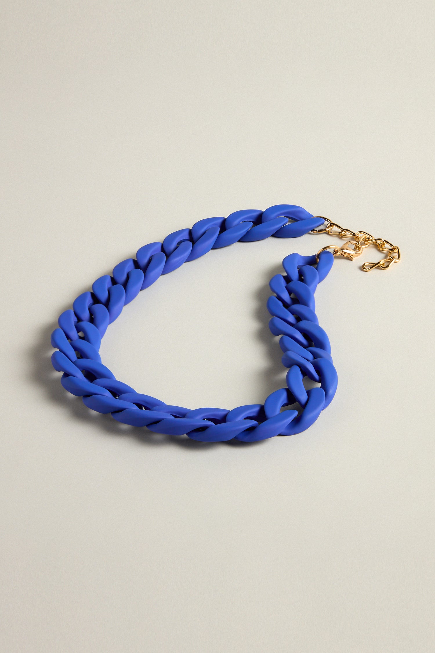 The Colour Pop Link Necklace, featuring a vibrant blue chain and an adjustable gold clasp, makes a bold statement on any plain surface.