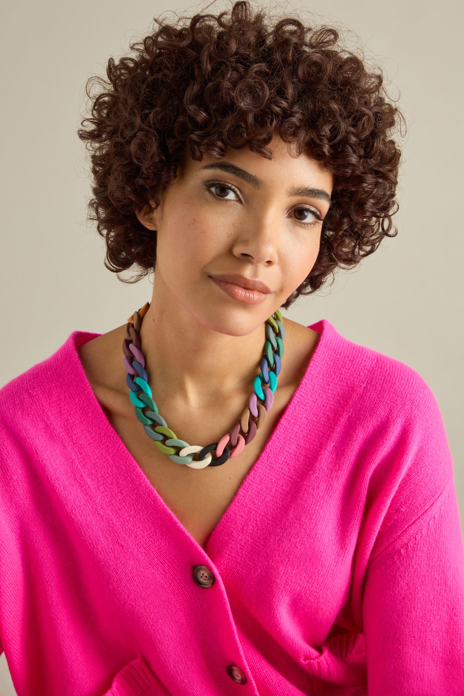 A person with curly hair wears the vibrant Colour Pop Link Necklace, a statement piece that perfectly complements their bright pink cardigan.